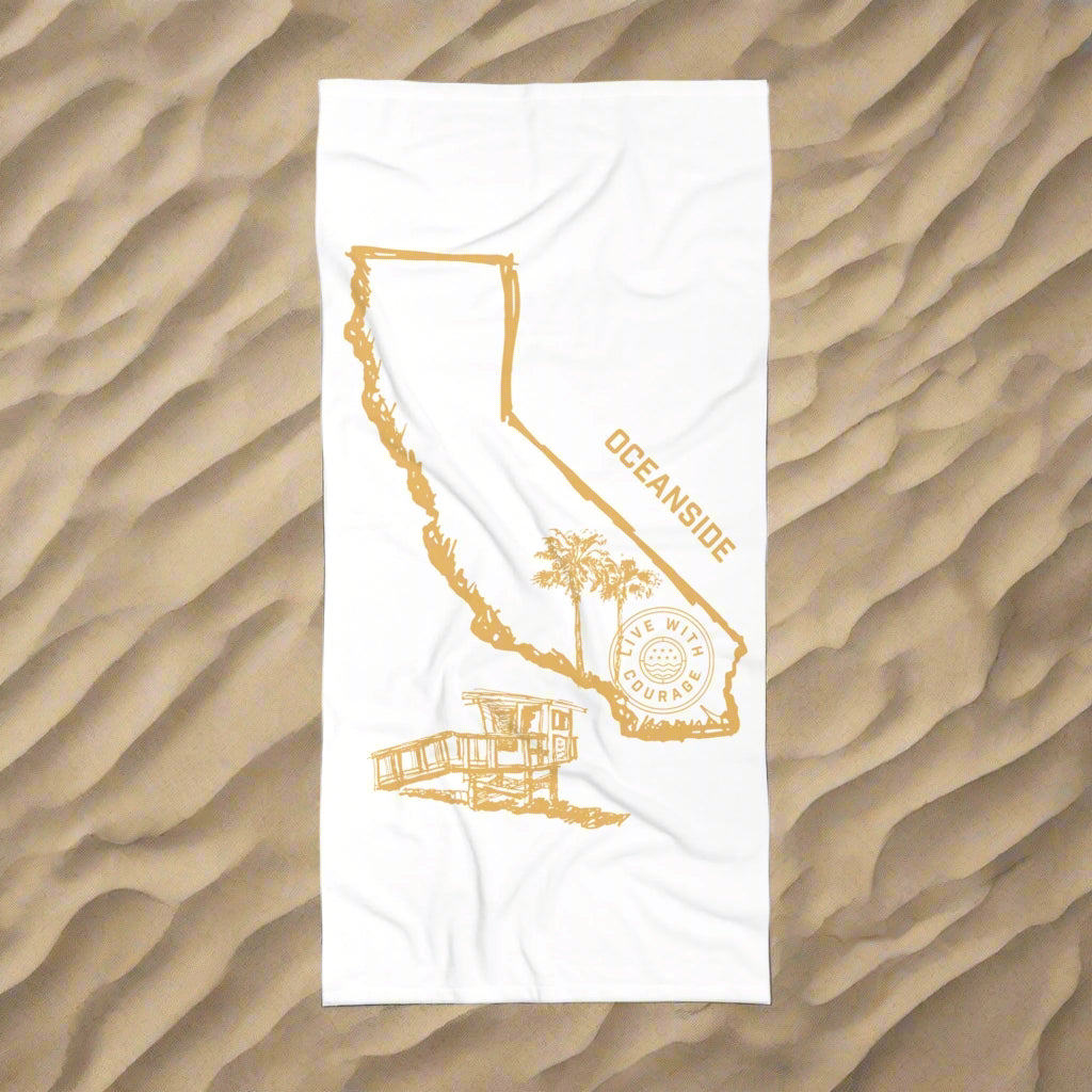 A white beach towel with a gold and orange print depicting the state of California, displayed on a wooden chair on a beach.