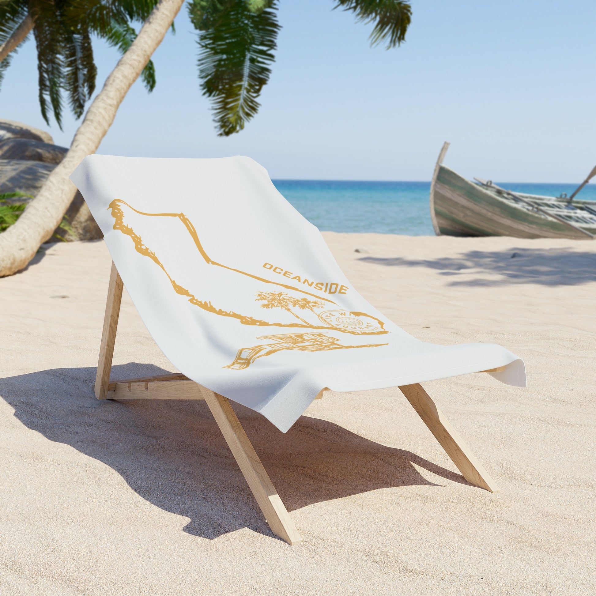 A white beach towel with a gold print depicting the state of California, and the city name of Oceanside displayed on a wooden chair on a beach.