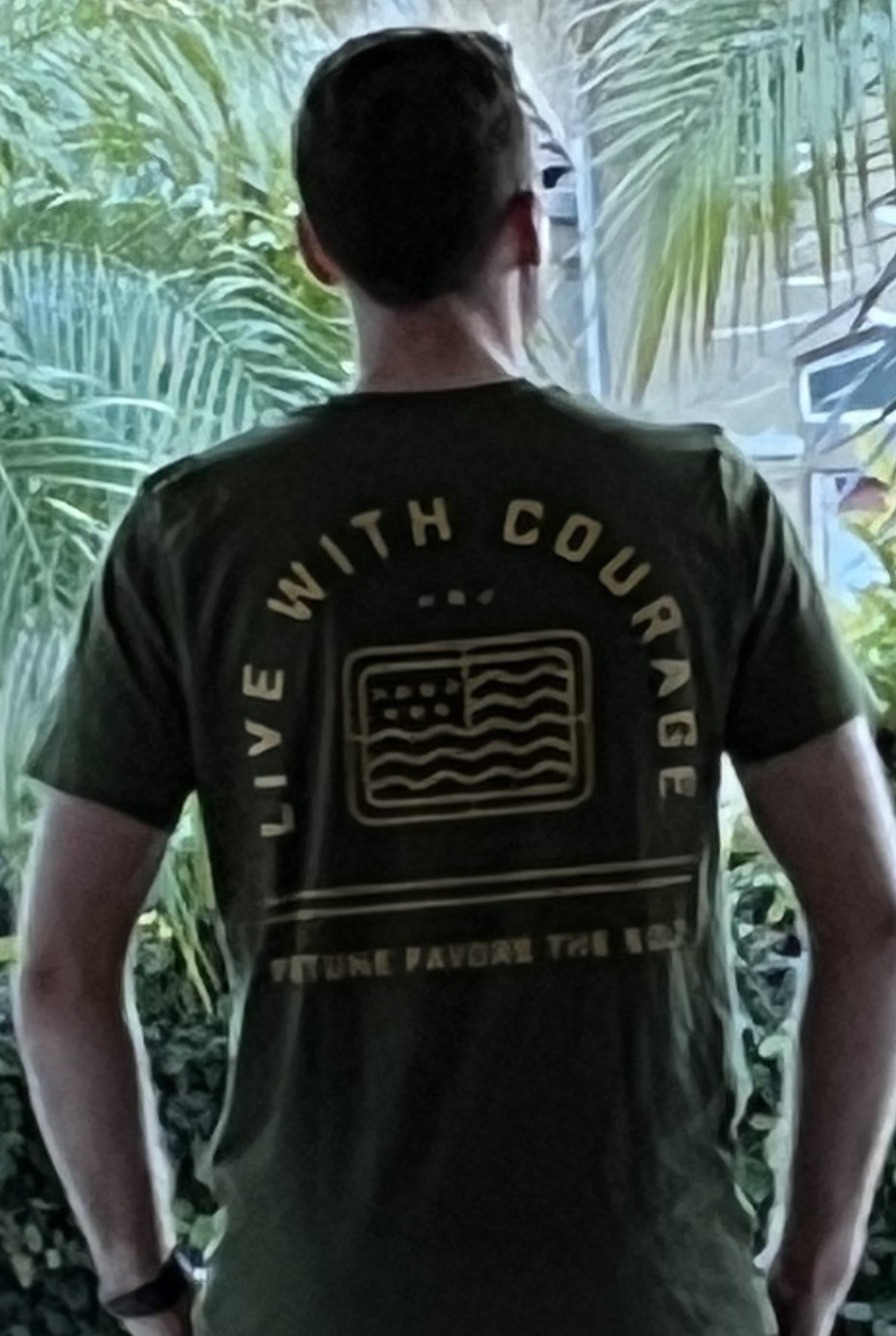 A person wearing a green short sleeve t-shirt with 'Live With Courage' and 'Fortune Favors the Bold' logos on the back.