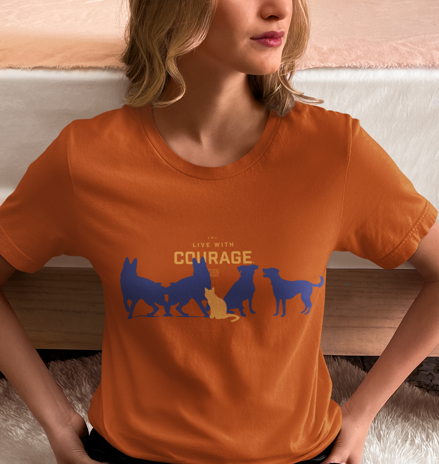Person wearing an orange t-shirt with dog silhouettes and 'Live with Courage' text.