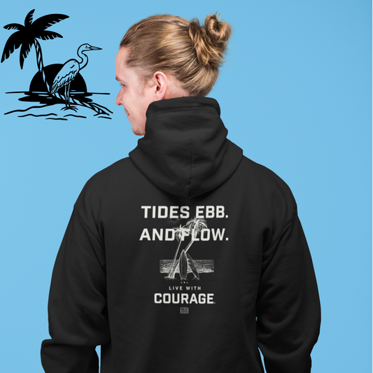 Person wearing a black hoodie with a beach scene and the words Tides Ebb and Flow with the Live With Courage®️logo.