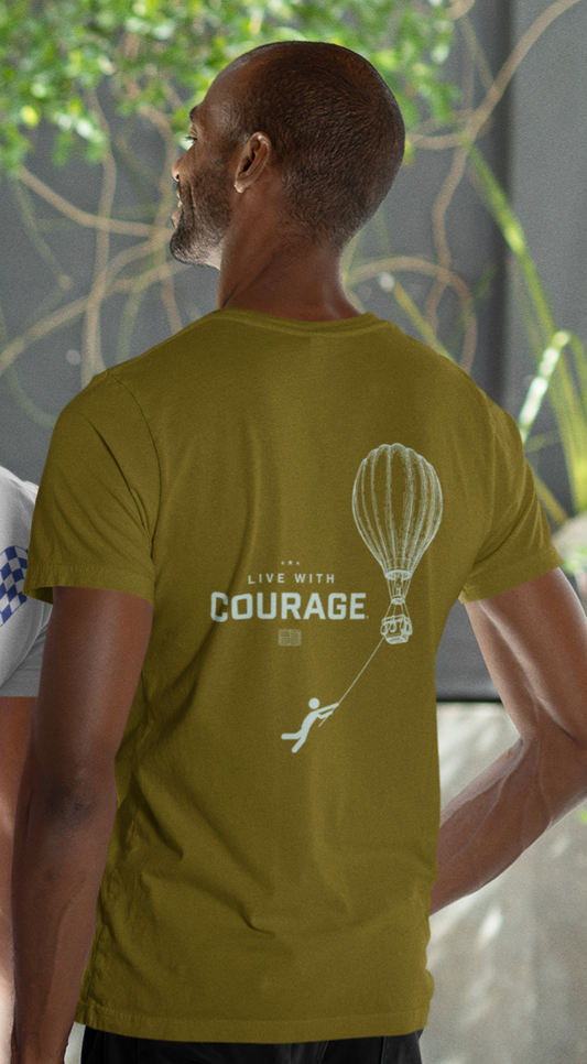 Person wearing a green t-shirt with 'Live with Courage' design on the back and a drawing of a hot air balloon in the air with a cartoon person hanging on below holding a rope.