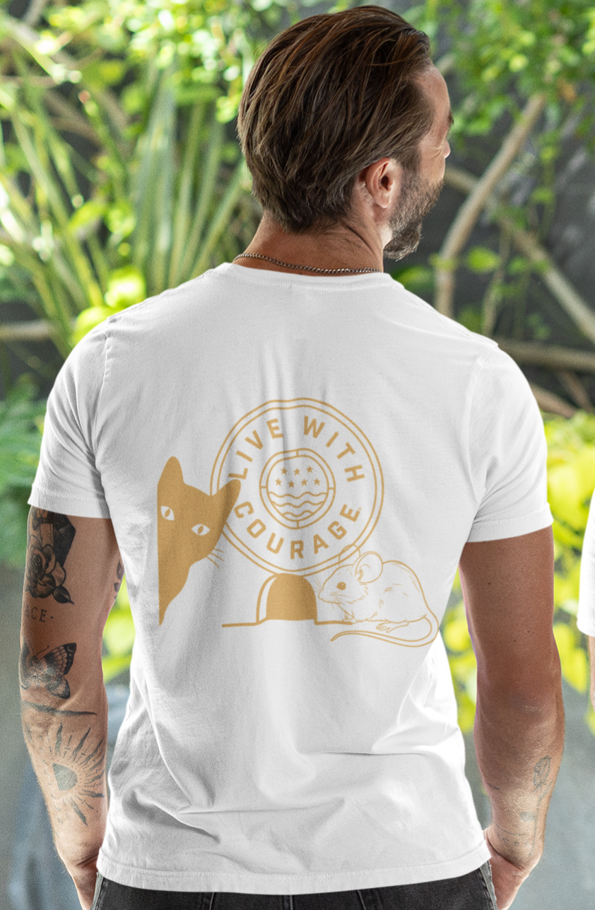 Man wearing a white t-shirt with a gold graphic of a cat and a mouse and text 'Live with Courage' outdoors.