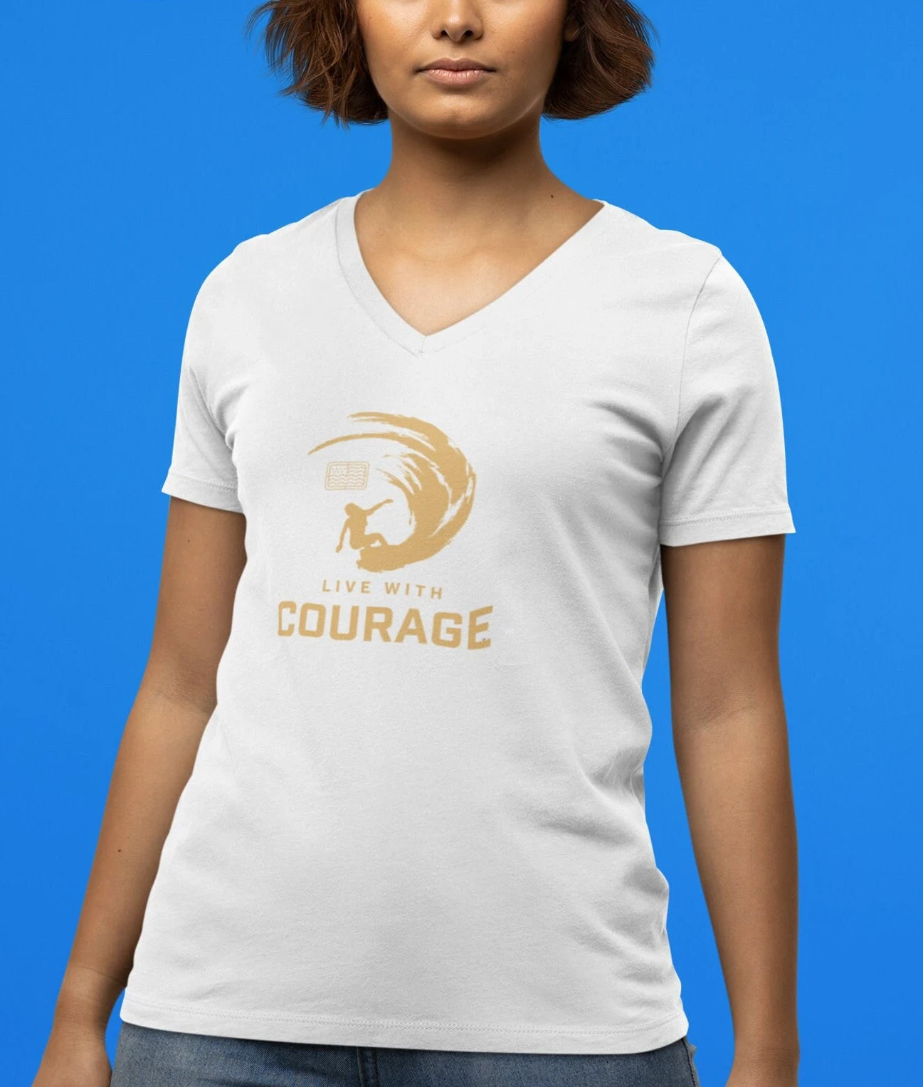 A woman wearing a white unisex short-sleeve V-neck t-shirt with a graphic that says 'COURAGE' and includes an image of a surfer girl carving a wave.