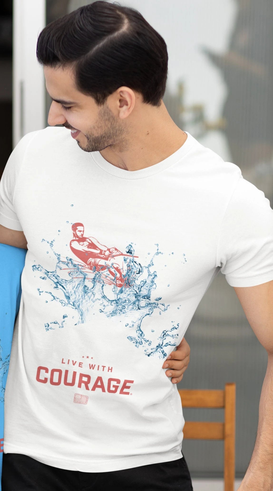 A person wearing a white unisex short sleeve tee with a graphic of a male slalom skier and the text 'Live With Courage' on the front.