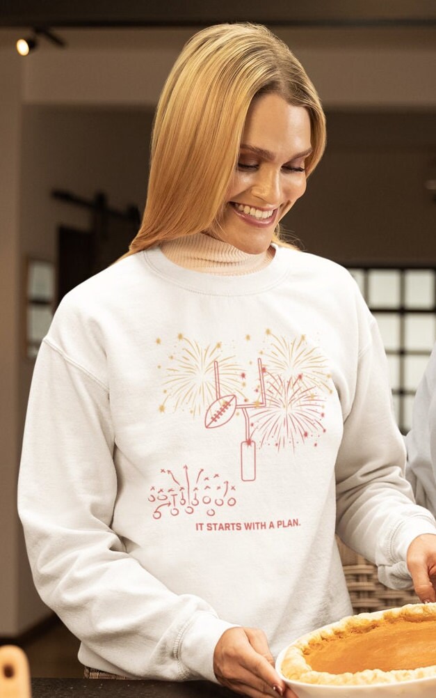A woman wearing a white sweatshirt with a football graphic and the text "It starts with a plan."