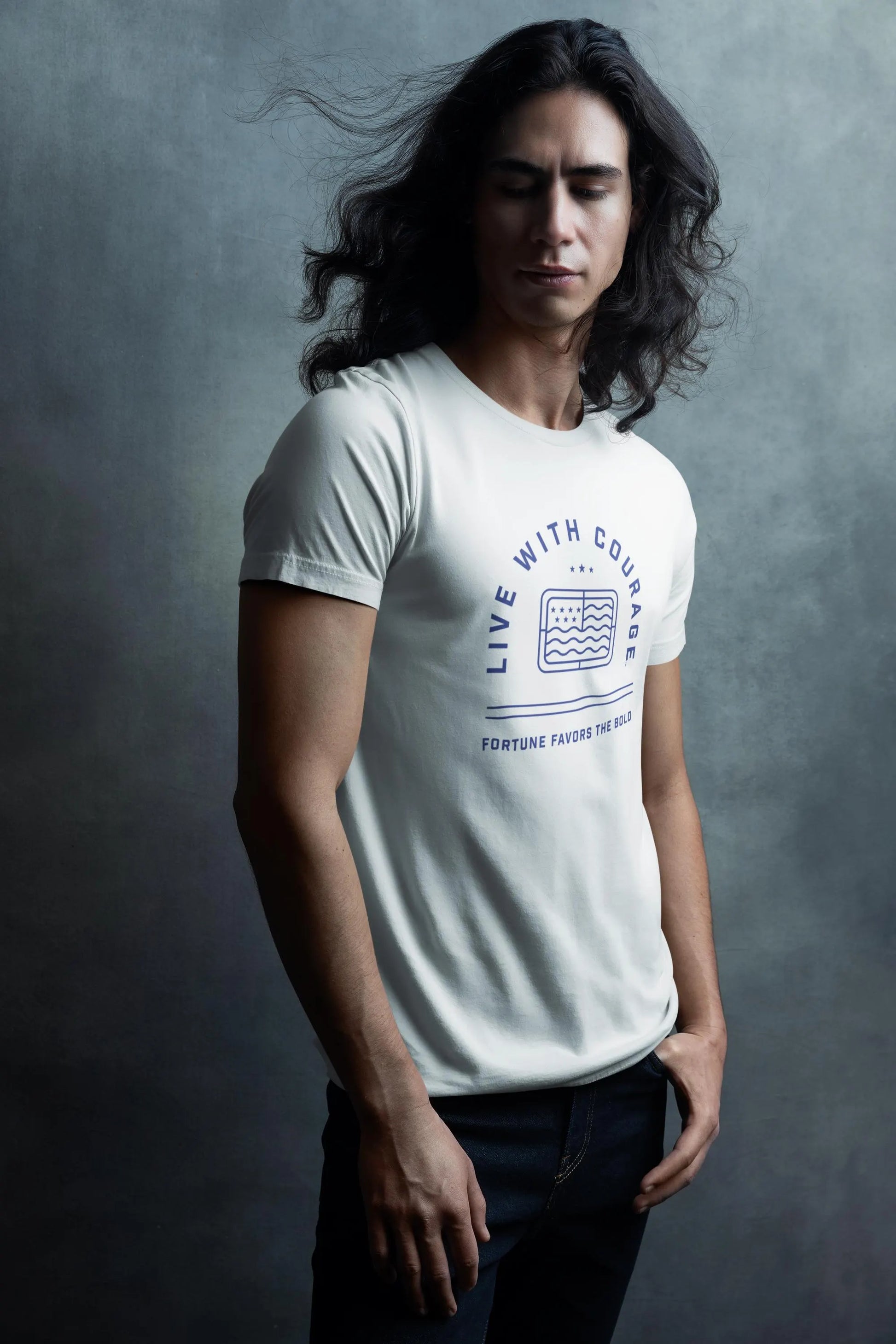 A person with long hair wearing a white short sleeve tee with the Live With Courage logo on the front.