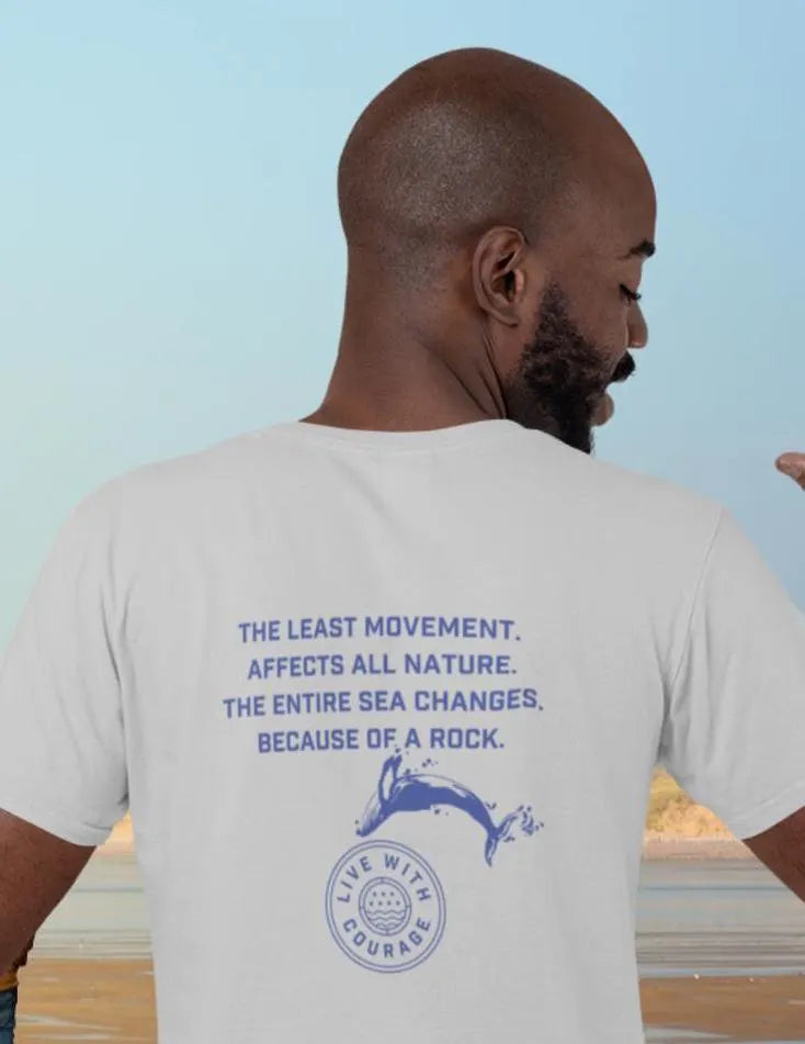 A person facing away from the camera wears a white unisex short sleeve tee with a quote from mathematician Blaise Pasqual and a whale jumping over the Live With Courage logo on the back.