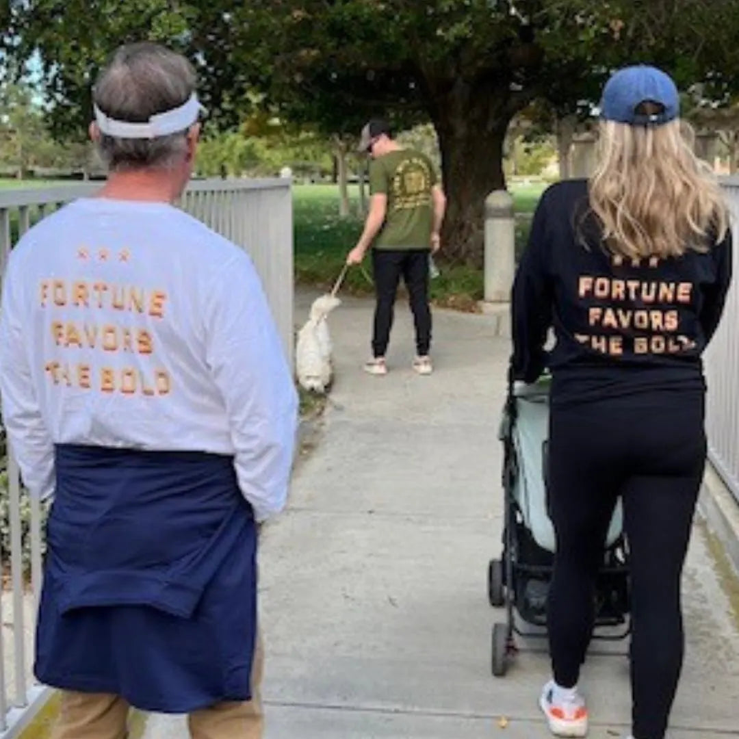 Two adults wearing long sleeve t-shirts with the text 'FORTUNE FAVORS THE BOLD' on the back, walking on a pathway.