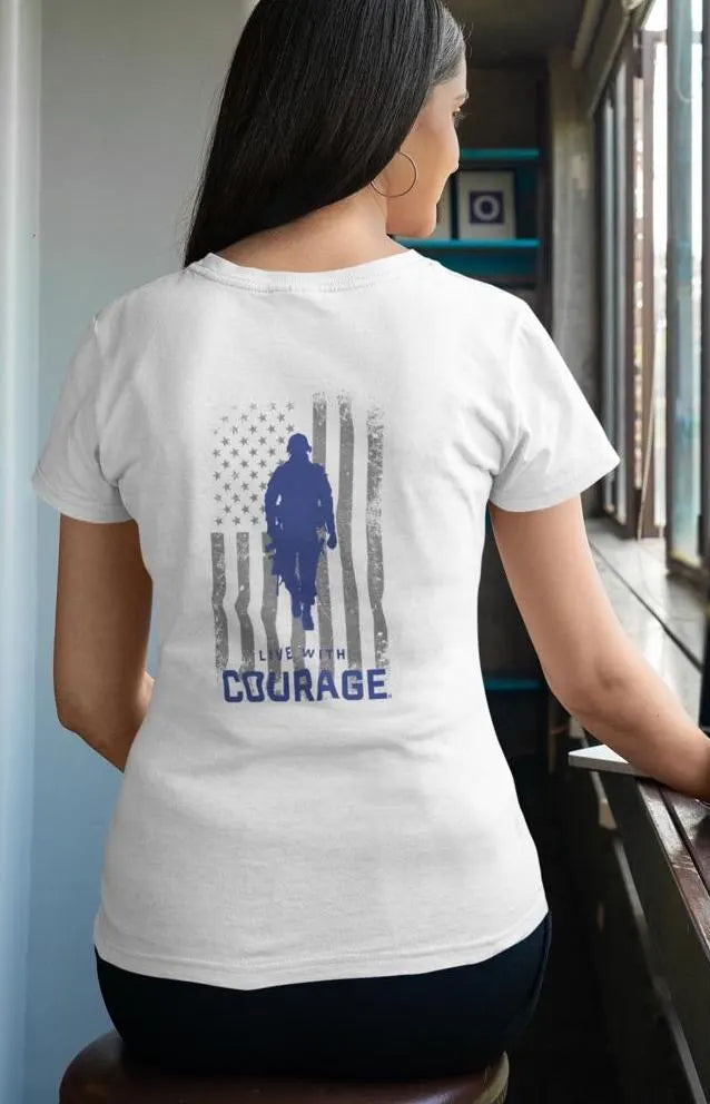 A woman facing away from the camera wears a white crew neck t-shirt with a graphic of a soldier and the American flag on the back, along with the text 'LIVE WITH COURAGE'.