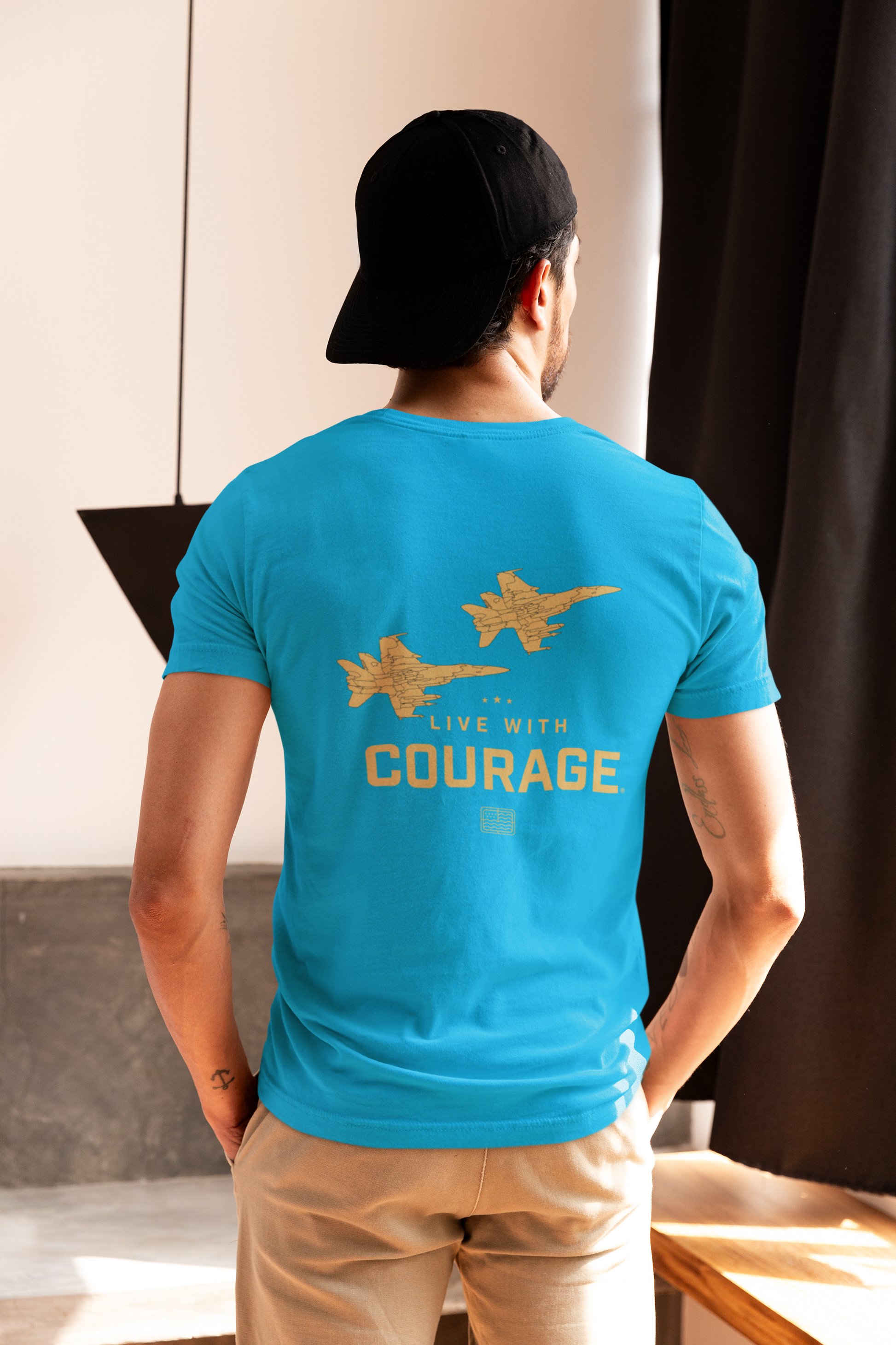 A man wearing a blue tee shirt with a graphic of two fighter jets and the words Live With Courage.