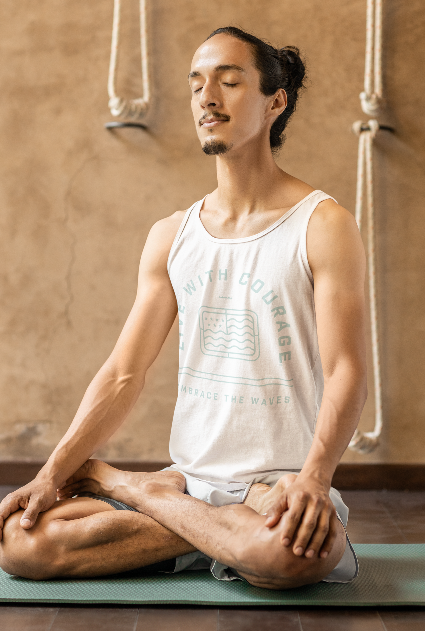 Man in a white tank top with the words Live With Courage and Fortune Favors the Bold practicing yoga in a studio setting.